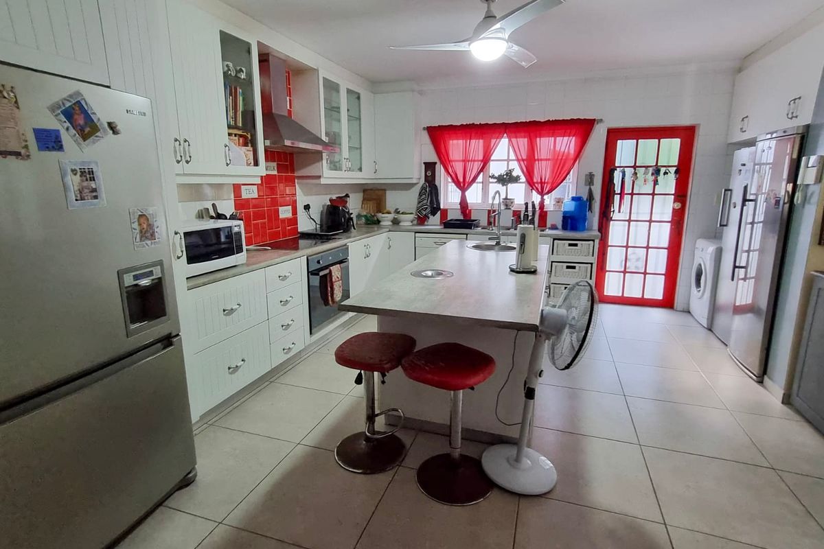 Spacious kitchen featuring a central island, white cabinetry, red tiled splashback, and direct access to the exterior through a glass-panelled door.