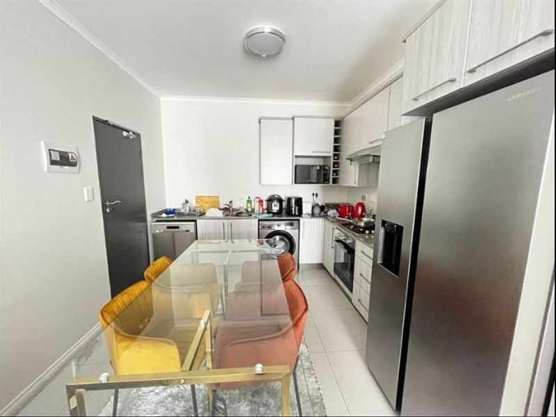 Open-plan kitchen featuring modern cabinetry, built-in oven, hob, and extractor fan, seamlessly integrated with the dining area on tiled flooring.