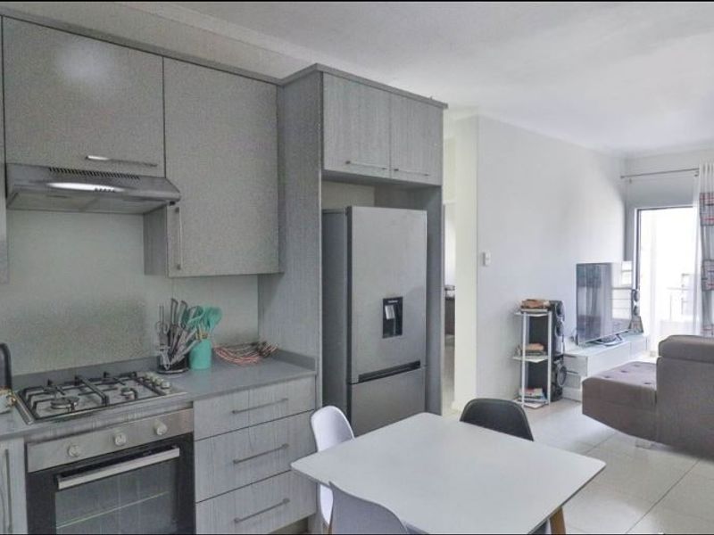 Modern open-plan kitchen and living area featuring contemporary grey cabinetry, gas hob, integrated oven, and tiled flooring leading to a balcony.