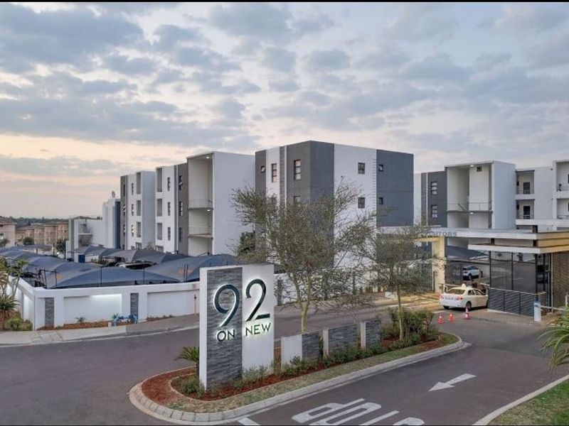 Front entrance view of the 92 on New apartment complex, featuring a secure gated access point, paved driveway, and modern multi-story residential buildings.