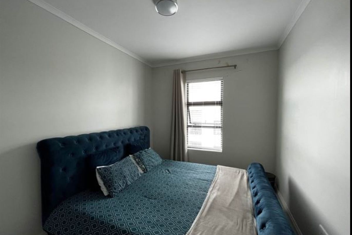 A standard bedroom featuring neutral walls, a ceiling light fixture, and a window with fitted blinds and a curtain rod.
