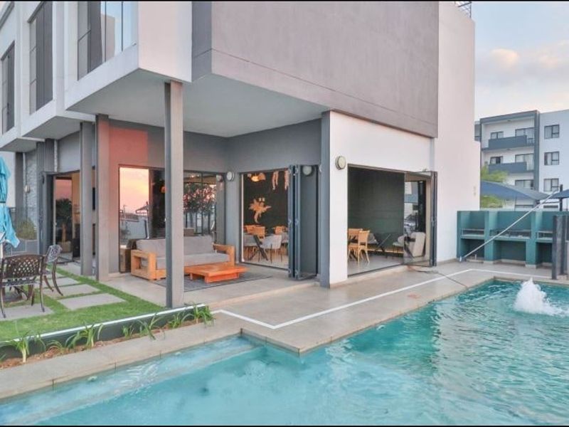 Modern apartment complex pool area featuring a swimming pool, built-in braai facilities, and seamless indoor-outdoor flow through large bi-fold doors.