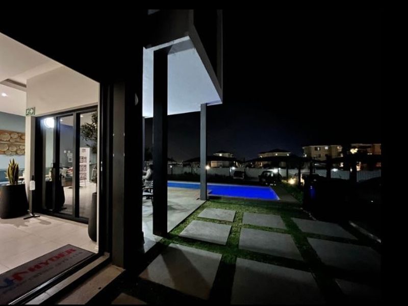 Night view of a modern apartment patio area featuring a swimming pool, paved walkway, and seamless indoor-outdoor flow through sliding glass doors.