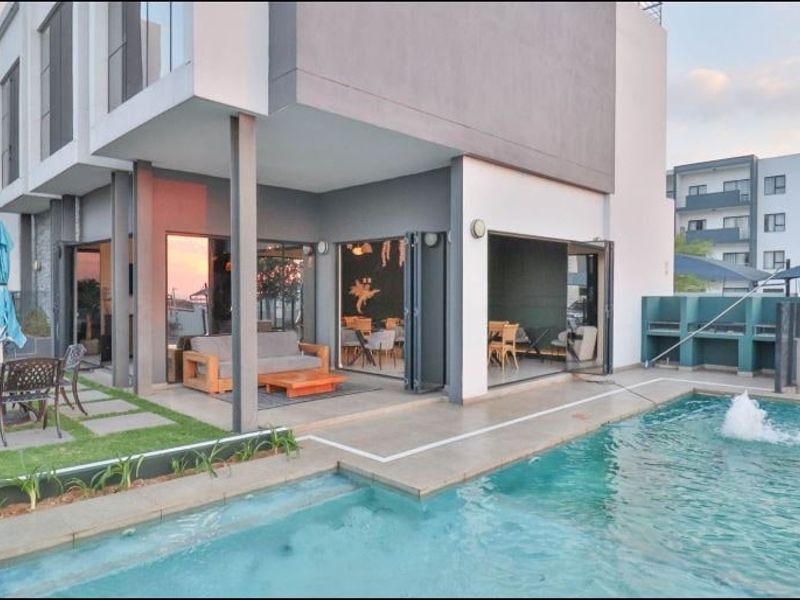 Modern apartment complex pool area featuring a swimming pool, built-in braai facilities, and seamless indoor-outdoor flow through large folding glass doors.