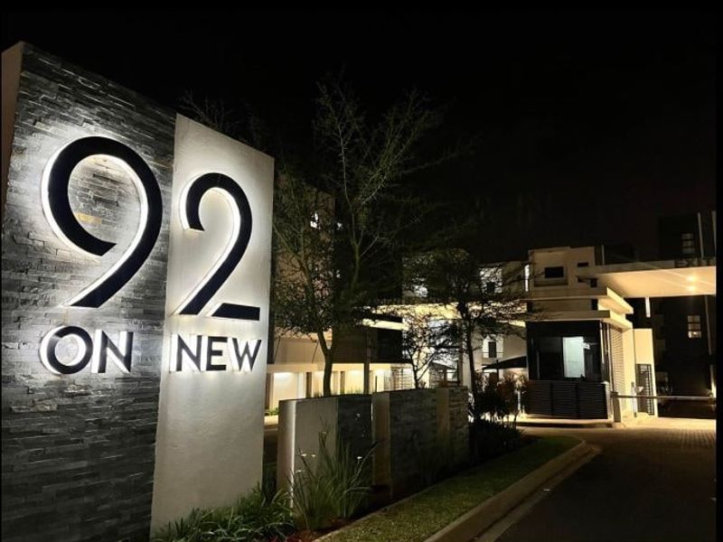 Night view of the modern apartment complex entrance featuring illuminated signage, stone cladding, and a secure gated access point.