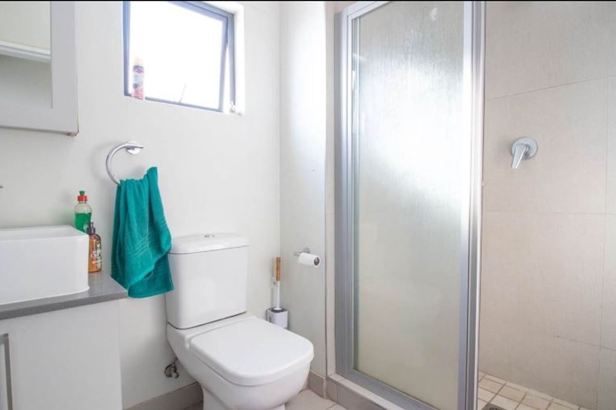 A functional bathroom featuring a modern vanity, a white toilet, and a glass-enclosed shower with neutral wall and floor tiling.