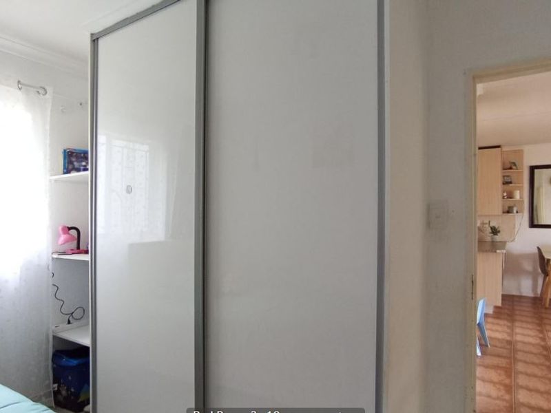 Bedroom featuring a modern built-in sliding door wardrobe and tiled flooring, with a view through to the adjacent living and kitchen area.