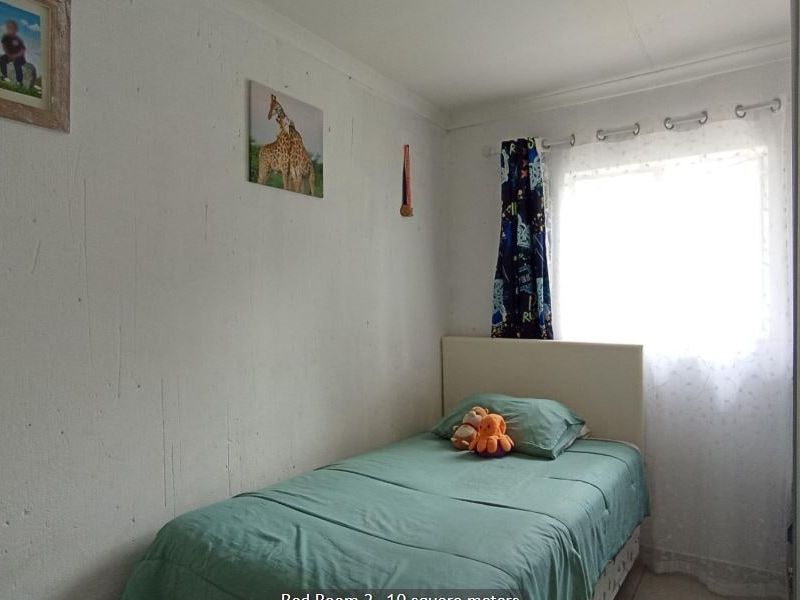 A compact bedroom featuring a built-in wardrobe and a window with security bars, requiring minor wall repairs and cosmetic updates.
