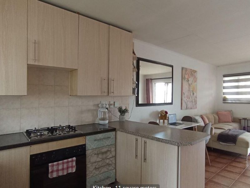 Open-plan kitchen and living area featuring light wood cabinetry, gas hob, under-counter oven, and direct access to an outdoor space via sliding doors.