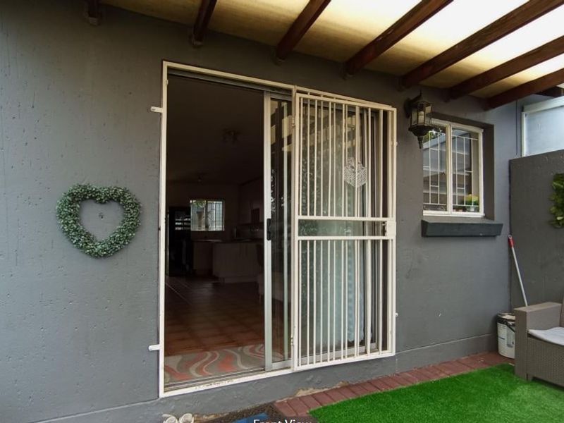 Covered patio area featuring a sliding glass door with security gate, timber pergola roof, and exterior wall lighting.