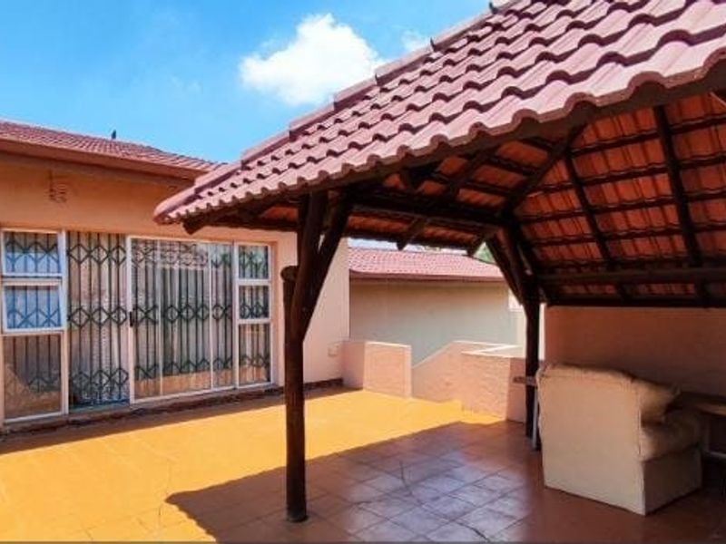 Covered outdoor patio area featuring tiled flooring and a rustic thatched roof structure, providing direct access to the home through a sliding glass door.