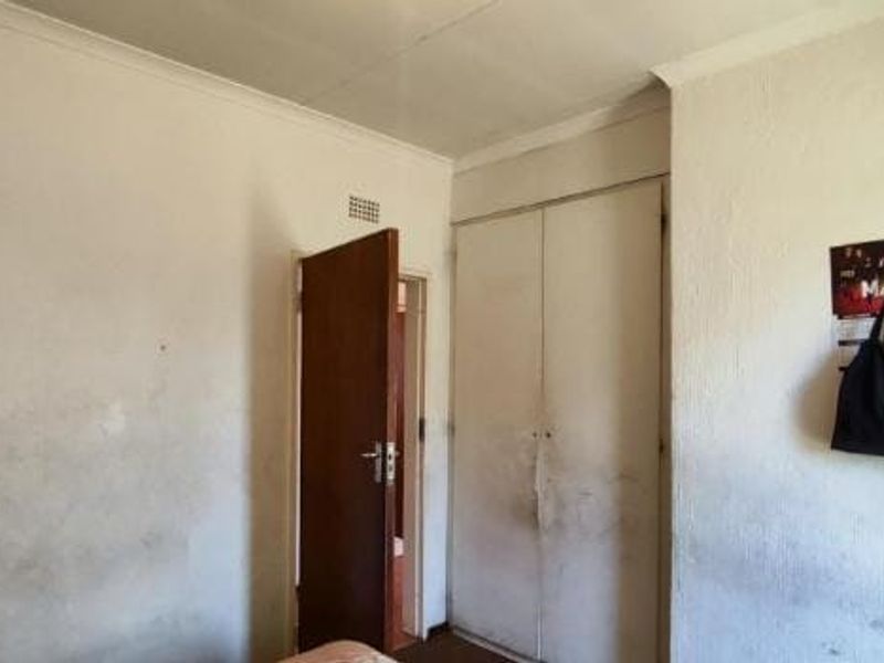 A bedroom featuring a built-in wardrobe and internal door, currently showing significant wear to the wall surfaces and finishes.