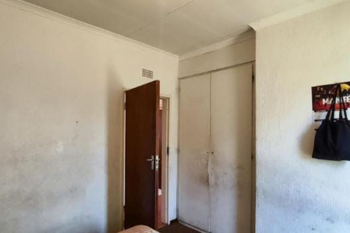 A bedroom featuring a built-in wardrobe and internal door, currently showing significant wear to the wall surfaces and finishes.