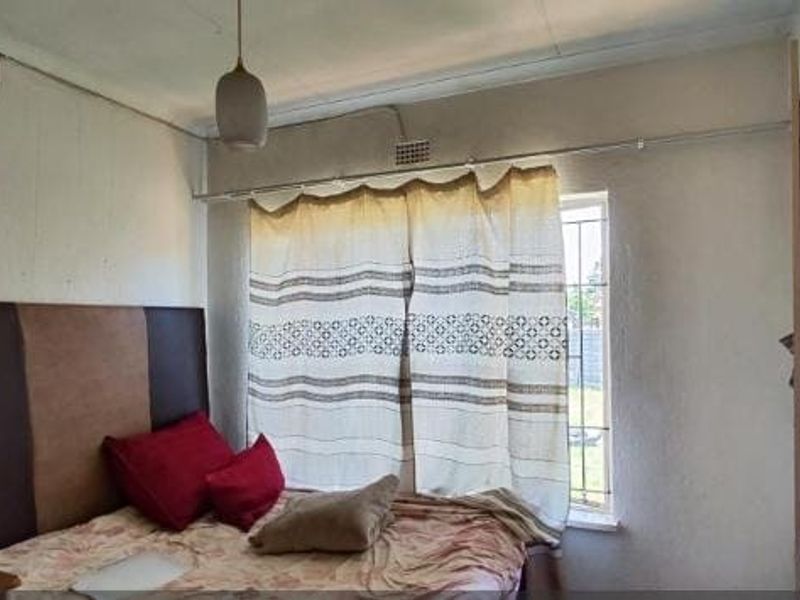 A bedroom featuring a built-in wardrobe and security bars on the window, requiring cosmetic updates to the wall finishes.