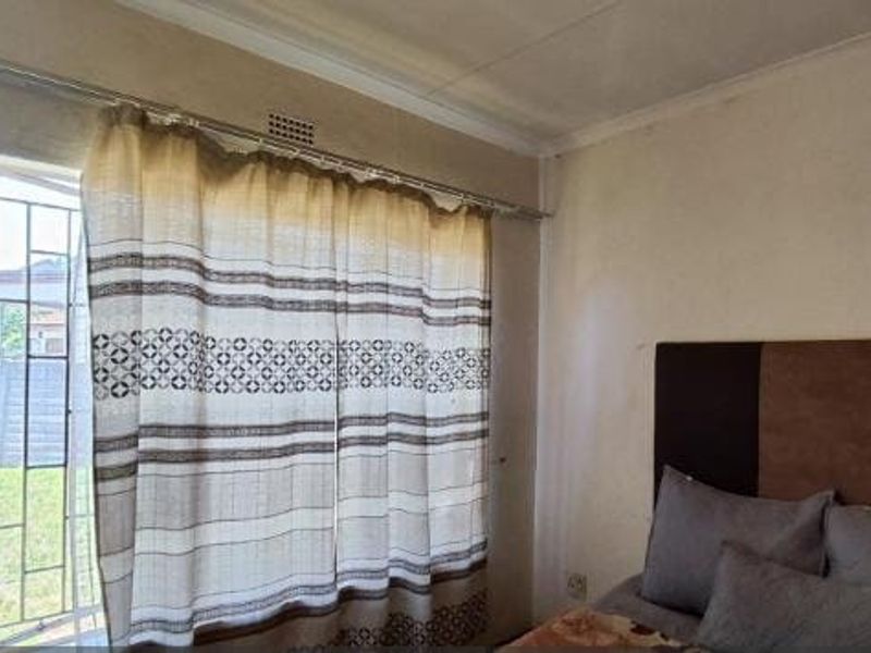A bedroom featuring a window with a security gate and curtain rail, showing signs of wear on the wall surfaces.