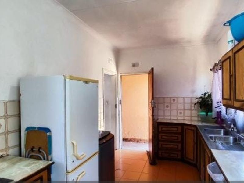 A functional kitchen featuring wooden cabinetry, tiled splashbacks, and a double bowl stainless steel sink, offering potential for modernization and cosmetic updates.