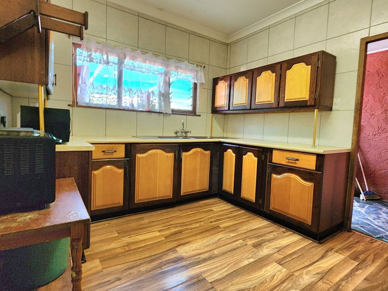 A dated kitchen featuring wood-tone cabinetry, laminate countertops, tiled splashbacks, and wood-look flooring, offering potential for a modern renovation.