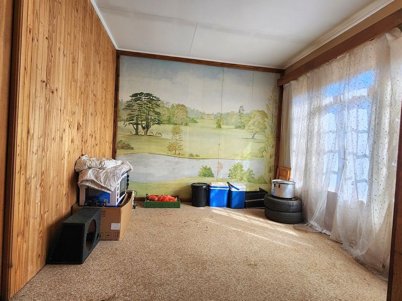 A living room featuring wood-paneled walls, carpet flooring, and a large window, offering a dated interior space ready for modernization.
