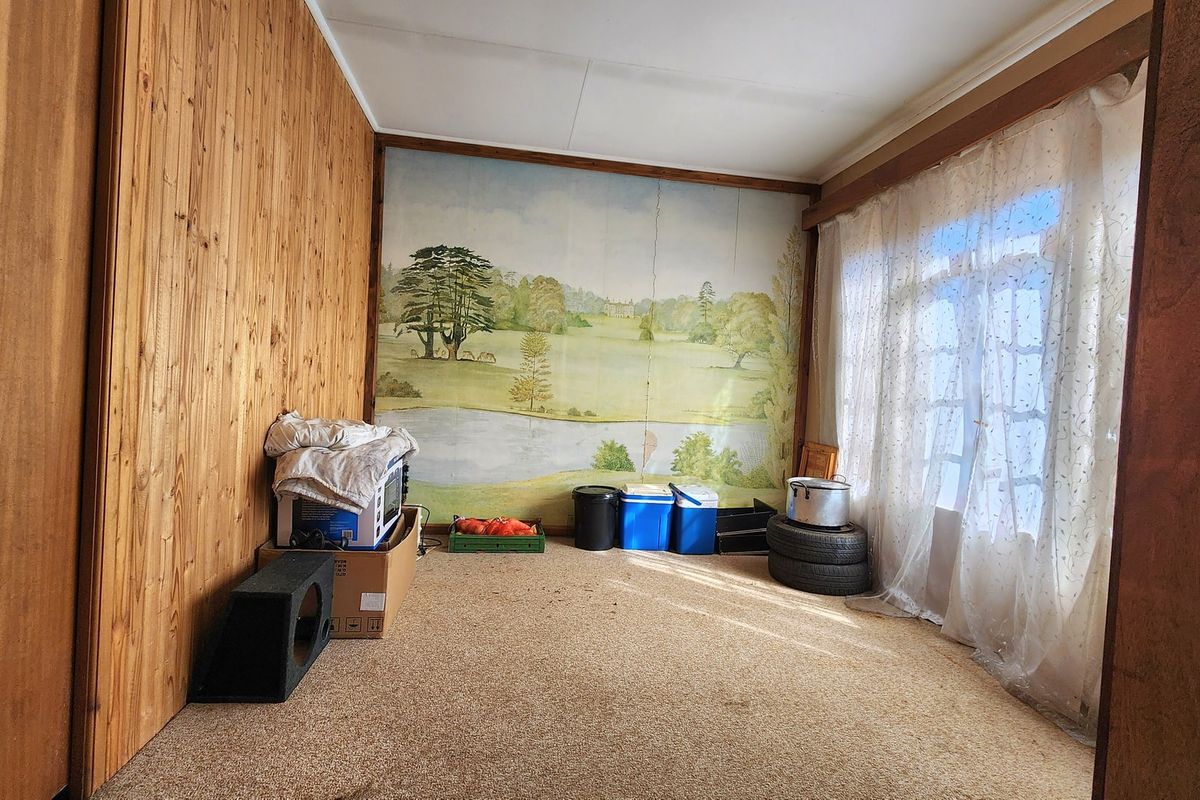 A living room featuring wood-paneled walls, carpet flooring, and a large window, offering a dated interior space ready for modernization.