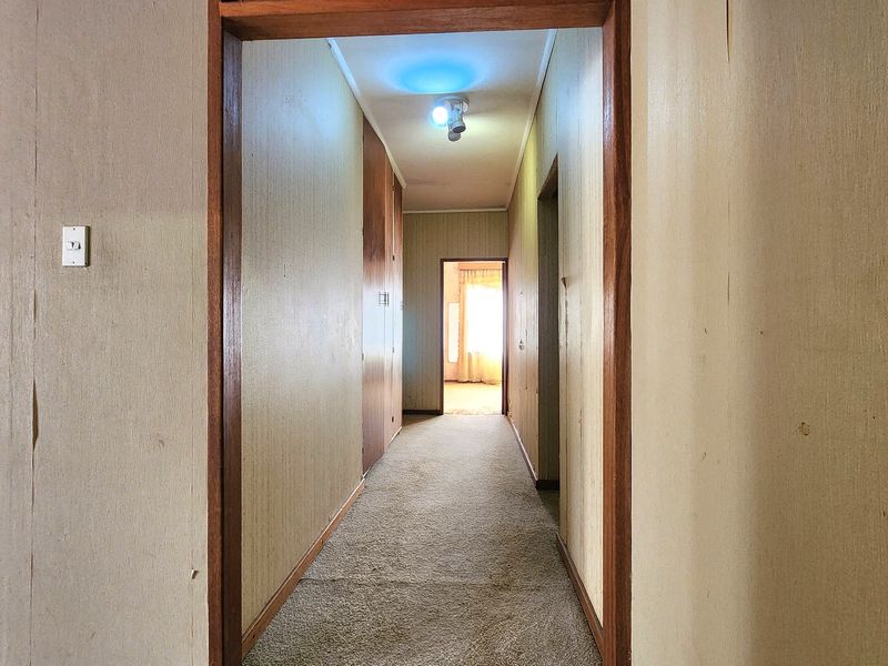 A functional hallway featuring built-in storage cupboards, timber door frames, and carpet flooring, presenting an opportunity for cosmetic updates.