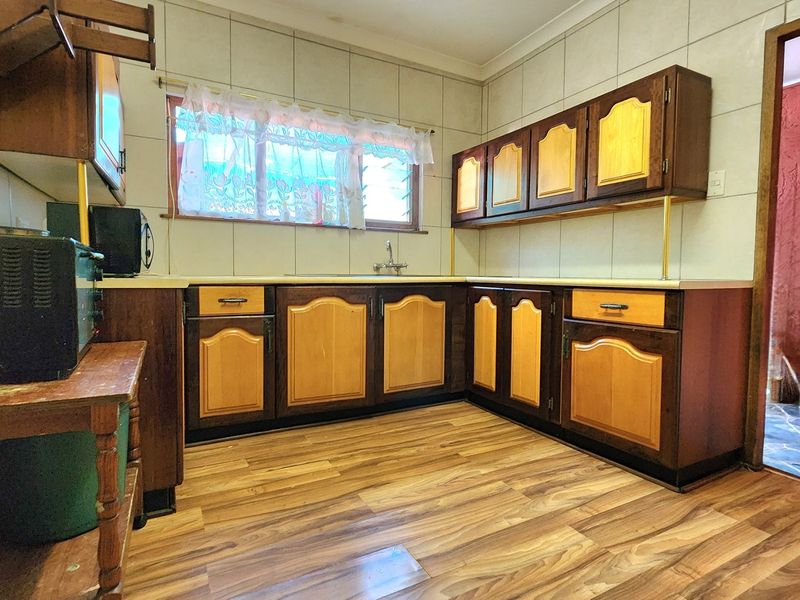 A dated kitchen featuring wood-tone laminate cabinetry, tiled splashbacks, and laminate flooring, offering potential for a modern renovation.