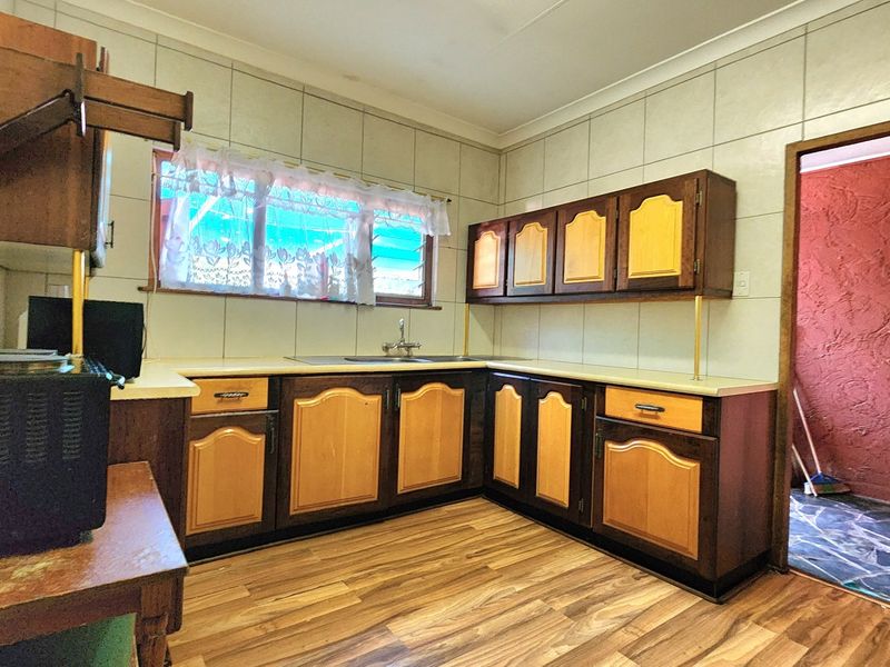 A dated kitchen featuring traditional laminate cabinetry, tiled splashbacks, and wood-look laminate flooring, offering significant potential for a modern renovation.