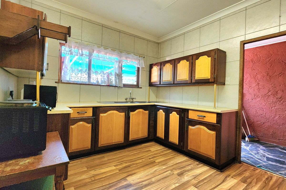 A dated kitchen featuring traditional laminate cabinetry, tiled splashbacks, and wood-look laminate flooring, offering significant potential for a modern renovation.