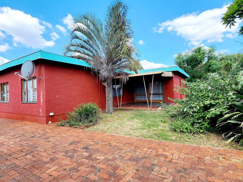 Front exterior view of a single-story house featuring a brick driveway, covered patio area, and mature garden landscaping.