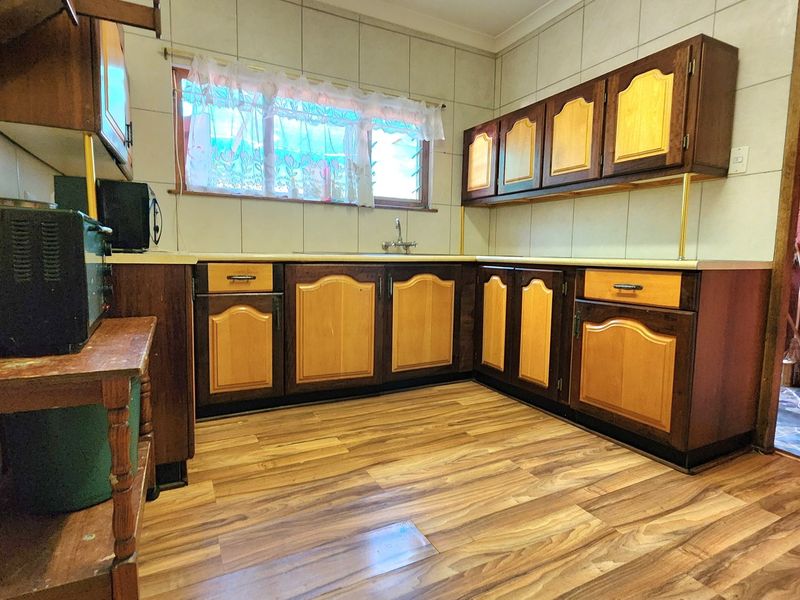 A dated kitchen featuring wood-tone cabinetry, laminate countertops, tiled backsplash, and wood-look laminate flooring, offering potential for a modern renovation.