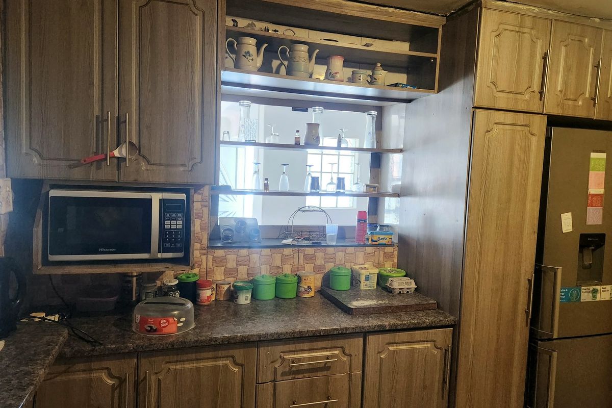 A dated kitchen featuring wood-look laminate cabinetry, tiled backsplash, and integrated microwave space, offering potential for a modern renovation.