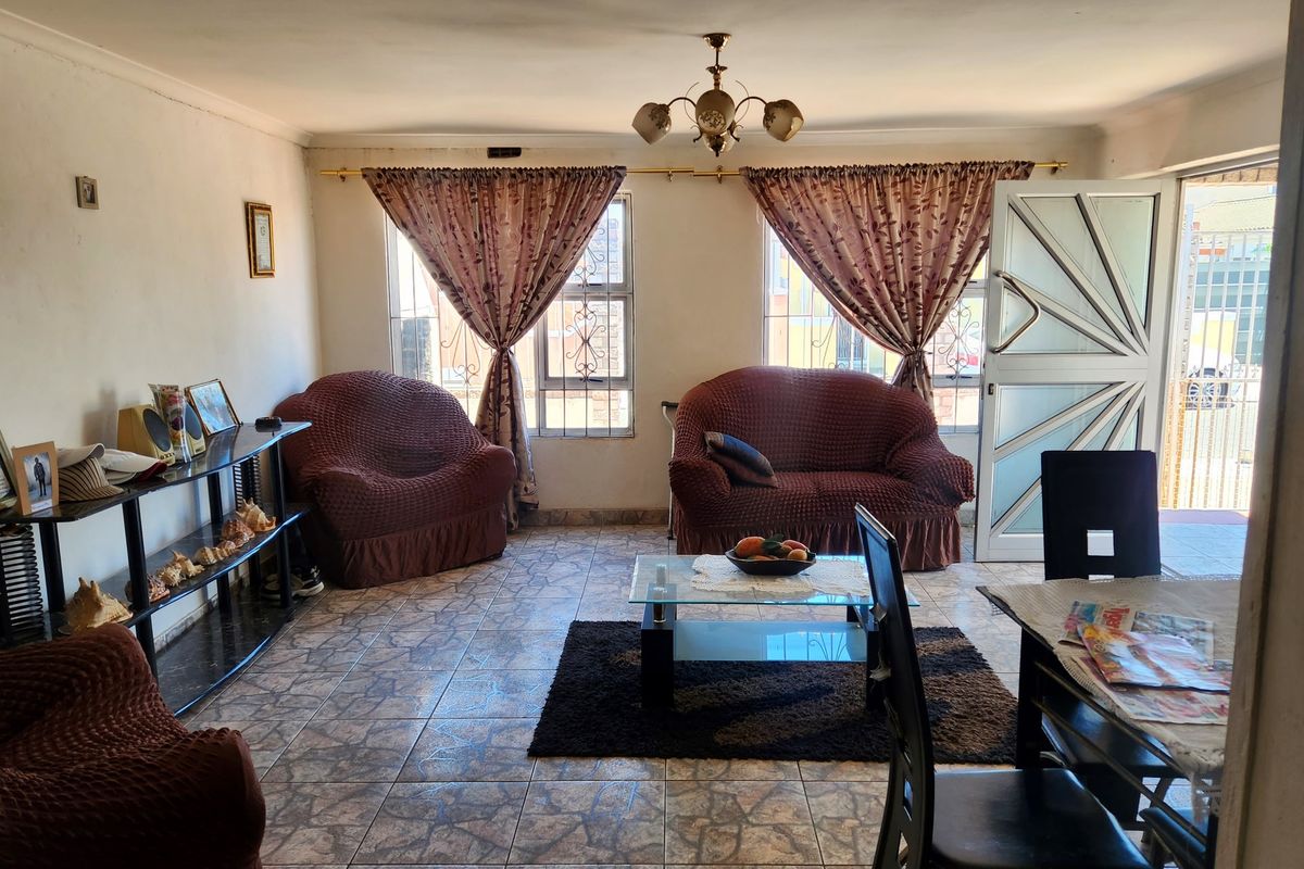 A living room featuring tiled flooring, a central ceiling light fixture, and direct access to the exterior through a security gate.