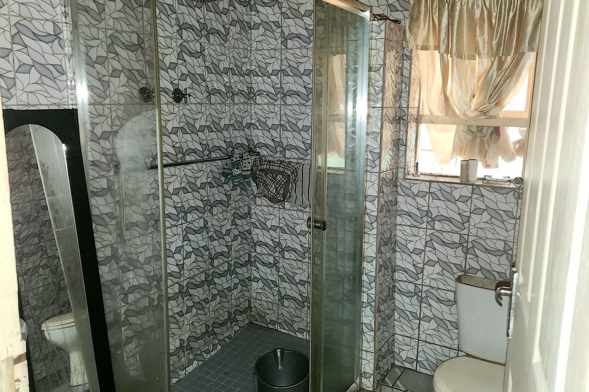 A compact bathroom featuring a glass shower enclosure, tiled walls and flooring, and a timber ceiling finish.