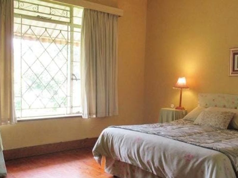A bedroom featuring timber flooring and a window fitted with security bars, offering a functional space with traditional finishes.