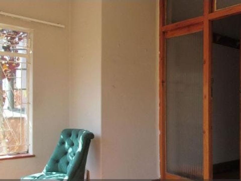 A sparsely furnished living area featuring a large window with security bars and a classic timber-framed glass door.