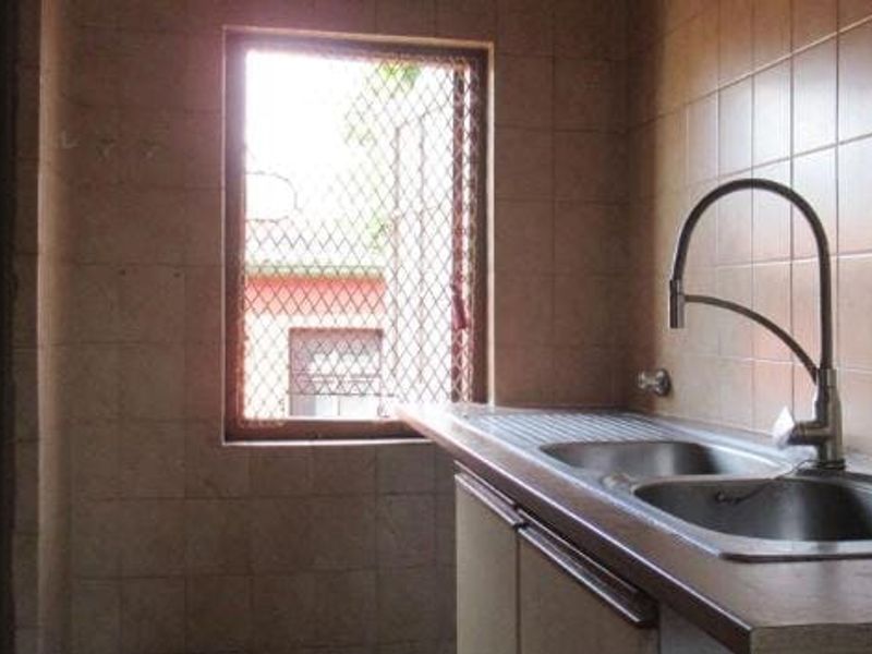 A functional scullery area featuring a double bowl stainless steel sink, gooseneck tap, and full-height wall tiling, ready for a modern update.
