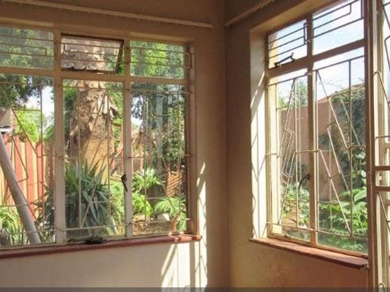An empty living area featuring large steel-framed windows with security bars, offering views of the garden and natural light.