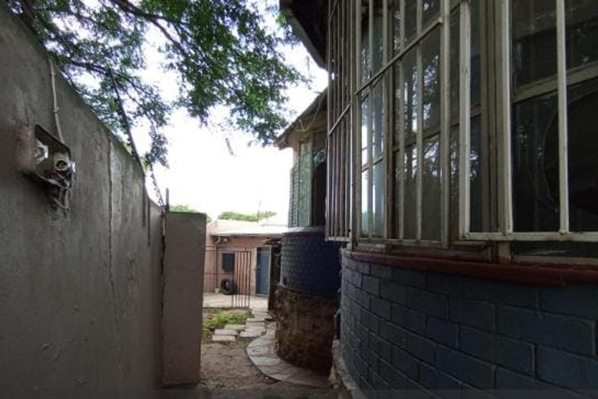 A narrow side passage showing a boundary wall with exposed wiring, stone-clad exterior wall, and security-barred windows.