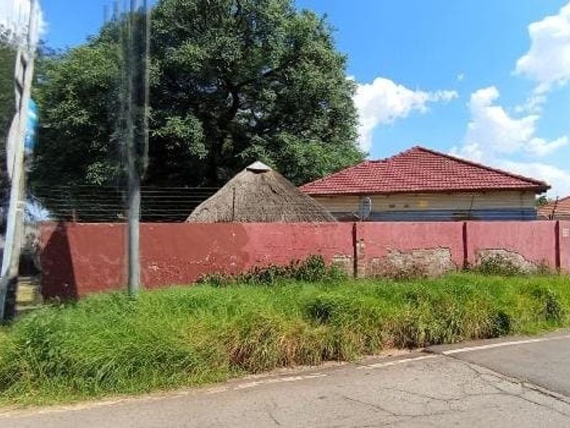 Street view of the property showing the perimeter wall with electric fencing and glimpses of the main dwelling's roof structures.