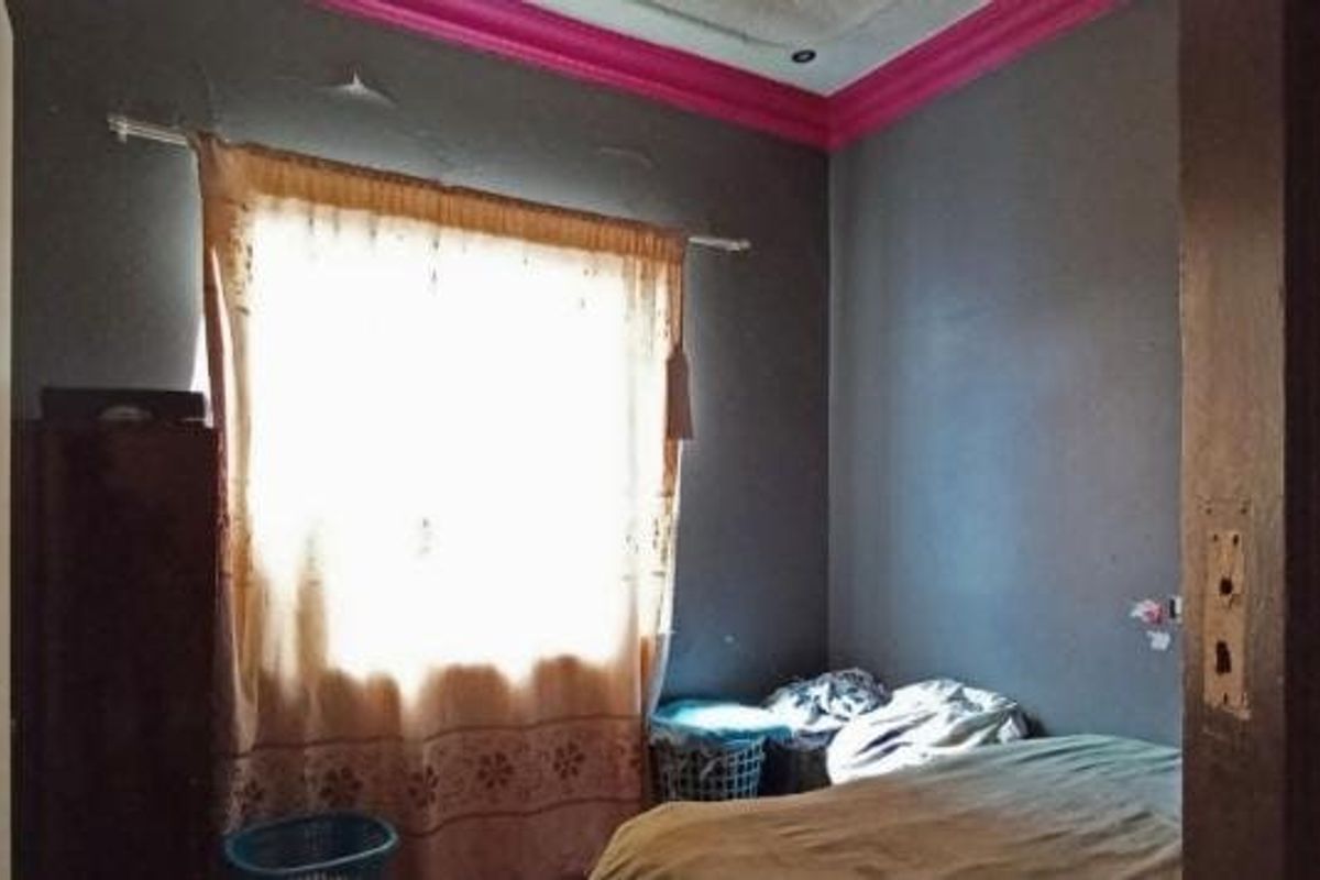 A bedroom featuring a built-in wardrobe and decorative pink cornice, currently showing signs of wear including ceiling cracks and damaged wall finishes.