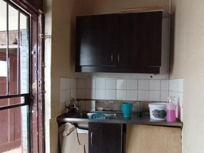 A small scullery or utility area featuring a stainless steel sink, tiled splashback, and dark built-in cabinetry, currently in need of maintenance and repair.