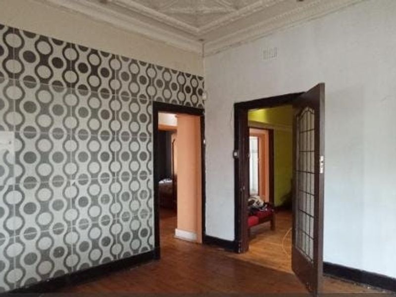 An empty living room featuring original ornate ceiling cornices, timber flooring, and distinctive patterned wall tiling, offering a blank canvas for renovation.
