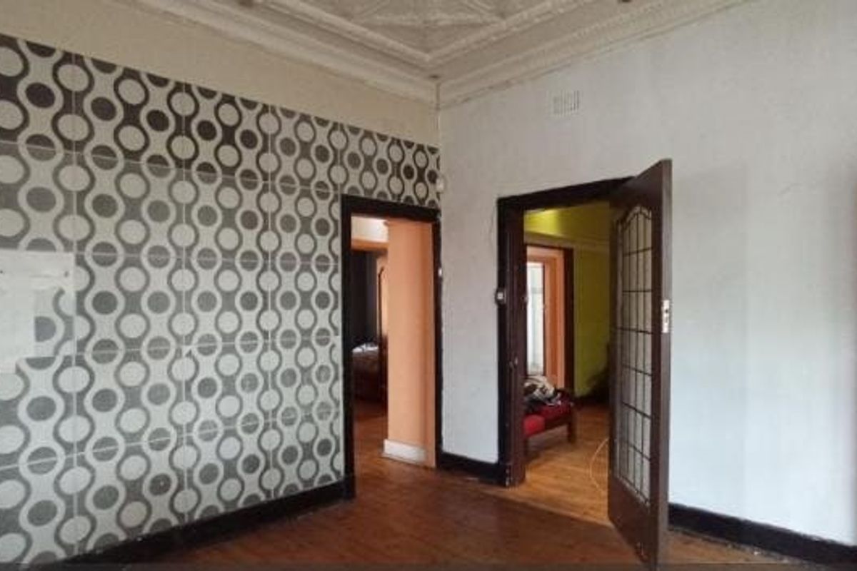 An empty living room featuring original ornate ceiling cornices, timber flooring, and distinctive patterned wall tiling, offering a blank canvas for renovation.