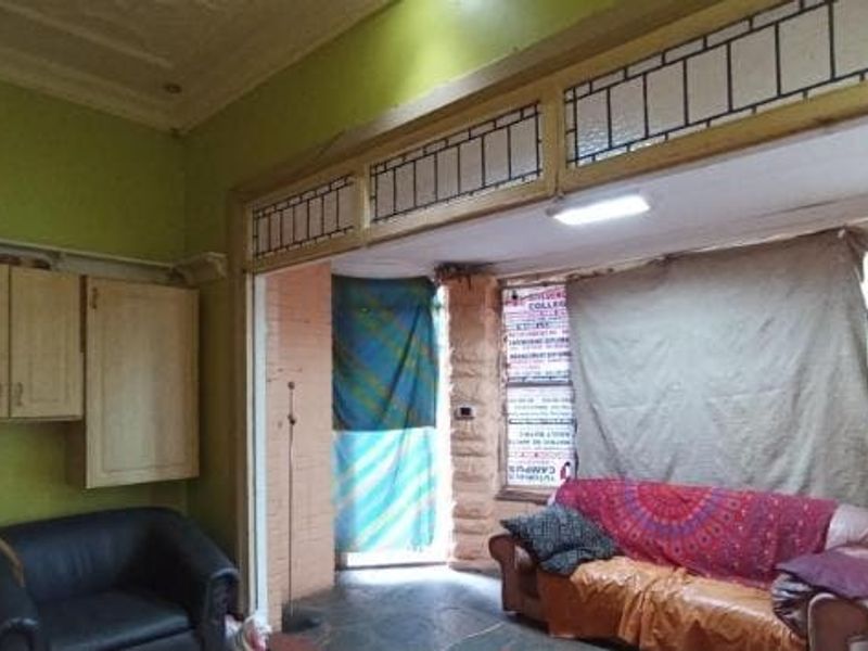 A living room featuring decorative ceiling molding, built-in cabinetry, and stone wall accents, currently requiring cosmetic updates and maintenance.