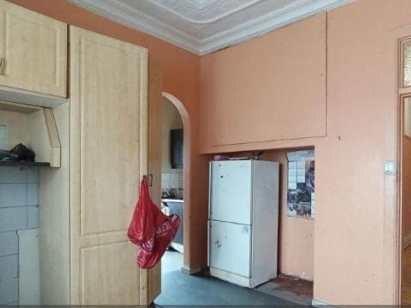 A dated kitchen area featuring built-in cabinetry, tiled splashbacks, and an ornate ceiling cornice, leading into a hallway with original wooden flooring.