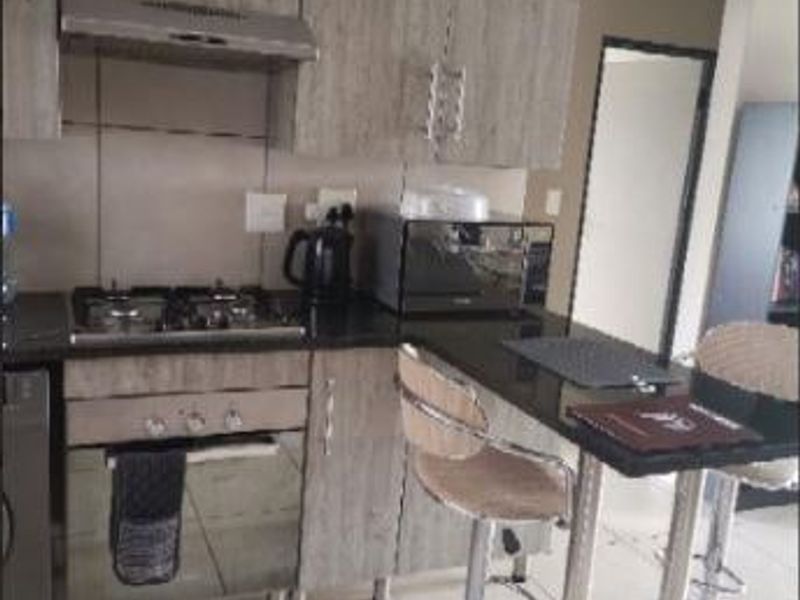 Compact modern kitchen featuring wood-look cabinetry, granite countertops, a gas hob, and an integrated breakfast bar area.