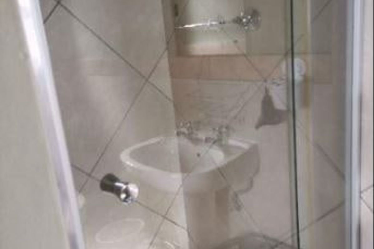 A compact bathroom featuring a pedestal basin, tiled finishes, and a glass-enclosed shower area.