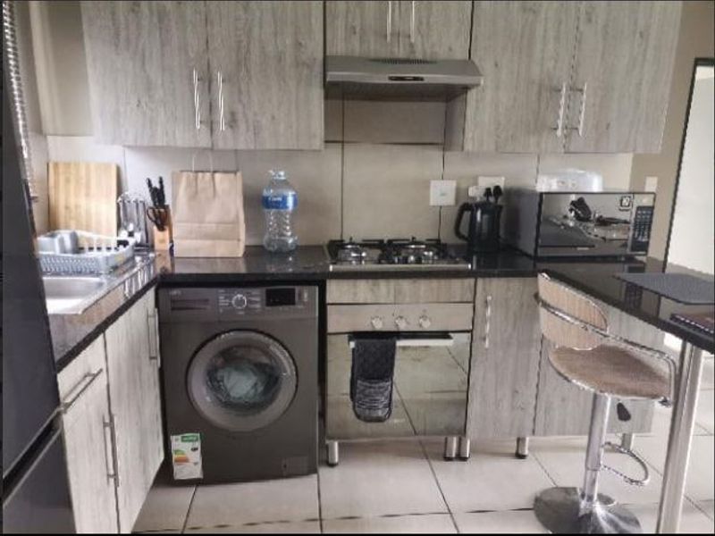 Compact modern kitchen featuring wood-look cabinetry, granite countertops, a gas hob, built-in oven, extractor fan, and integrated laundry space.