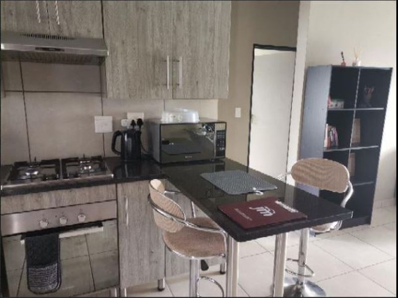 Compact kitchen featuring modern wood-look cabinetry, granite countertops, a built-in gas hob, oven, and an integrated breakfast bar for casual dining.