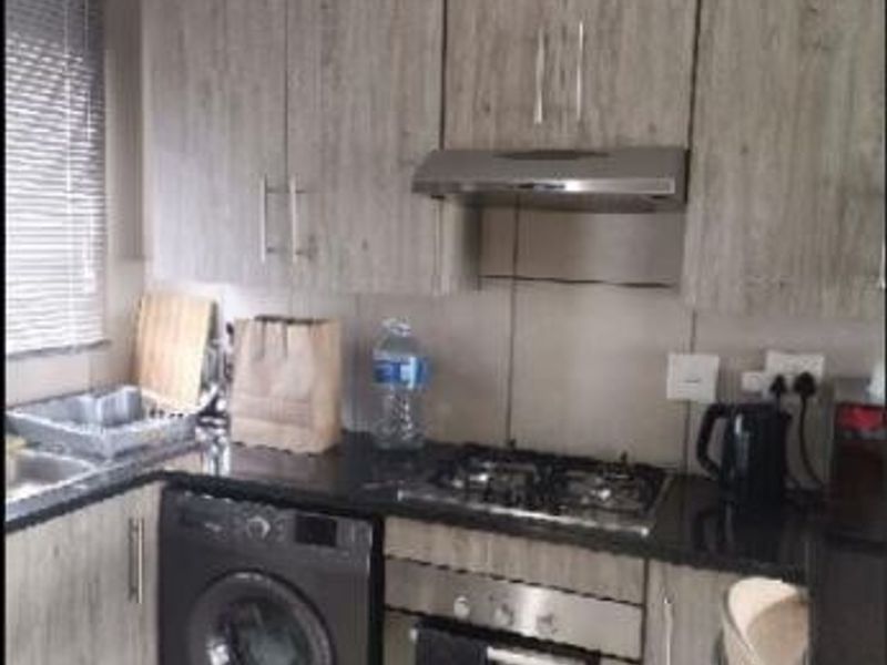 Compact kitchen featuring modern wood-look cabinetry, granite countertops, a gas hob, built-in oven, extractor fan, and an integrated washing machine.