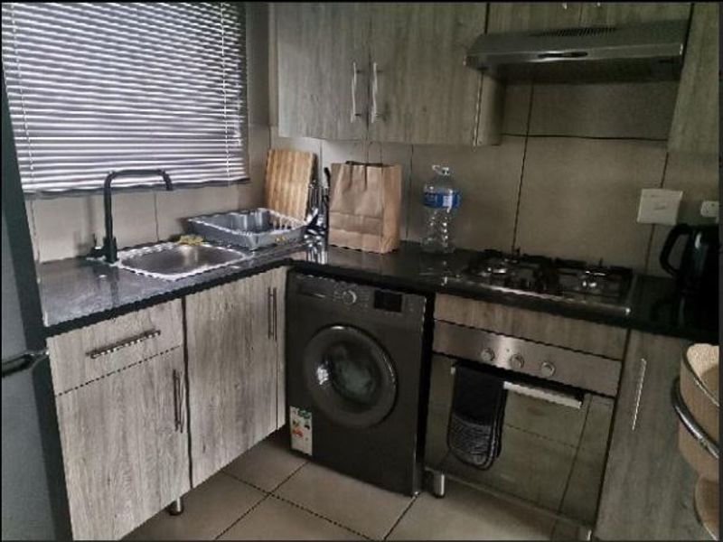 Compact kitchen featuring modern laminate cabinetry, granite countertops, built-in oven with gas hob, extractor fan, and an integrated washing machine.